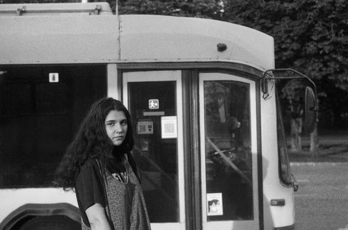Free Black and white photo of a young woman standing near a city bus. Stock Photo