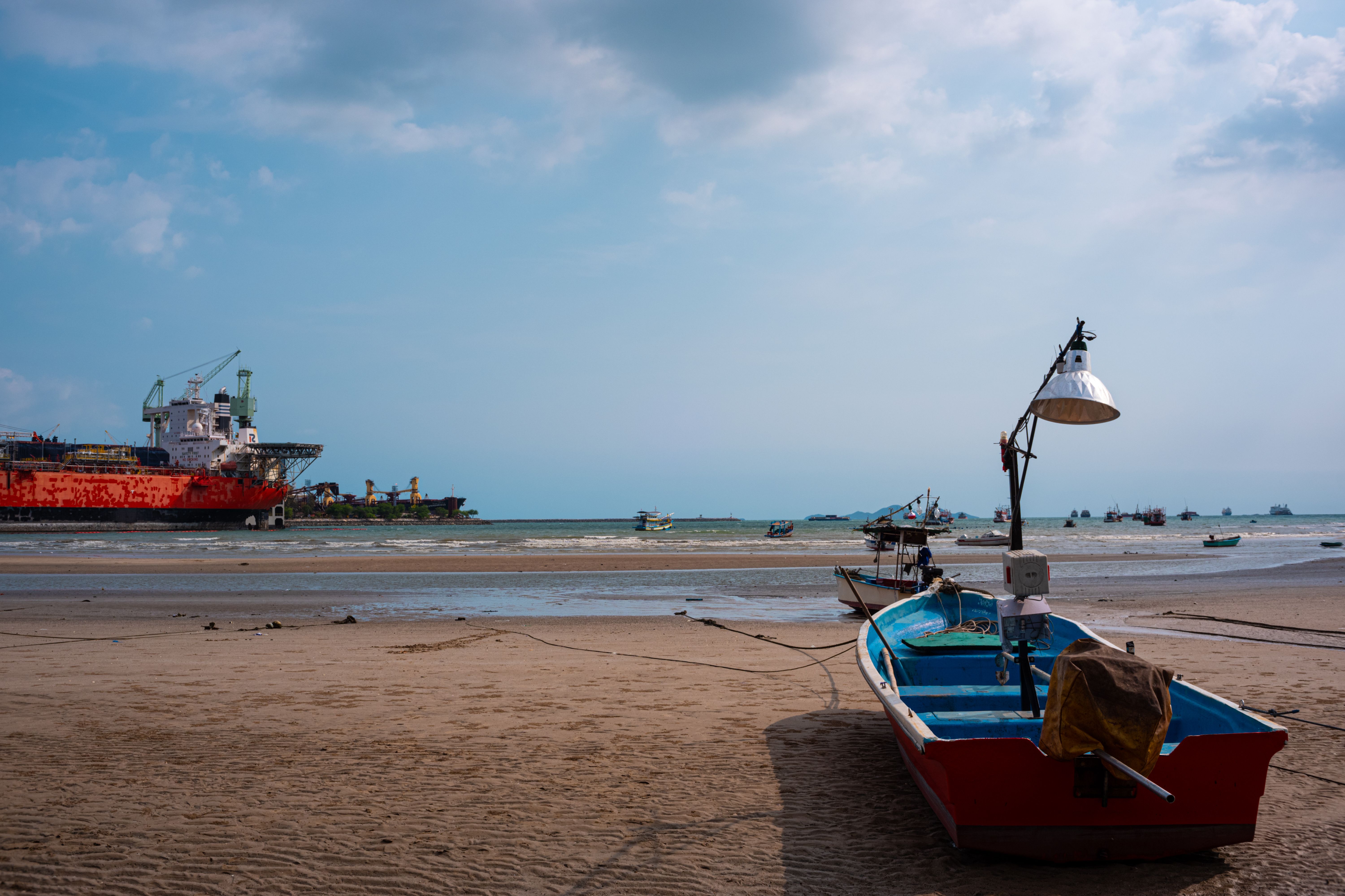 Stunning Pattaya beach view featuring fishing boats and a distant cargo ship under a bright blue sky.