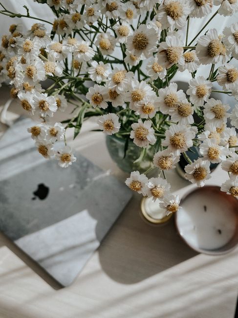 Charming white flowers in a vase on a desk with a laptop and candle. Perfect for serene interior decor inspiration.