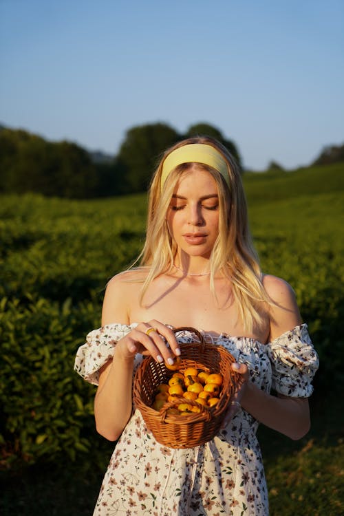 A Woman in Off Shoulder Floral Dress Holding a Basket of Fruits