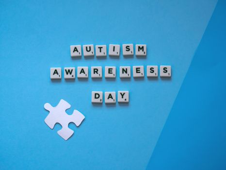 Autism Awareness Day concept with letter tiles and a puzzle piece on a blue background.