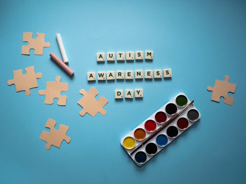 Letter Tiles beside Puzzle Cutouts and a Watercolor Set on a Blue Surface