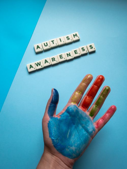 Free A top view of a colorful painted hand next to autism awareness scrabble tiles on a blue background. Stock Photo