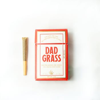 Flat lay of Dad Grass CBD joint and packaging on a white background.
