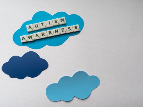 Flat lay of scrabble tiles spelling 'Autism Awareness' on blue cloud cutouts, ideal for awareness campaigns.