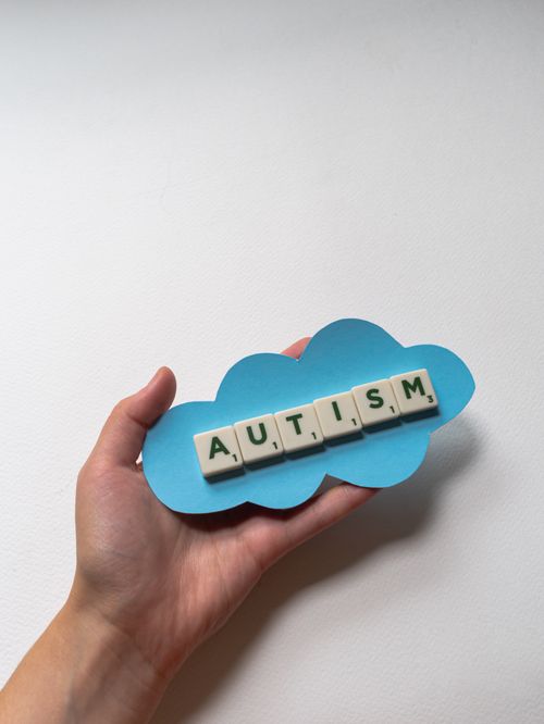 Free Close-up of a hand holding autism word tiles on blue cloud cutout. Stock Photo
