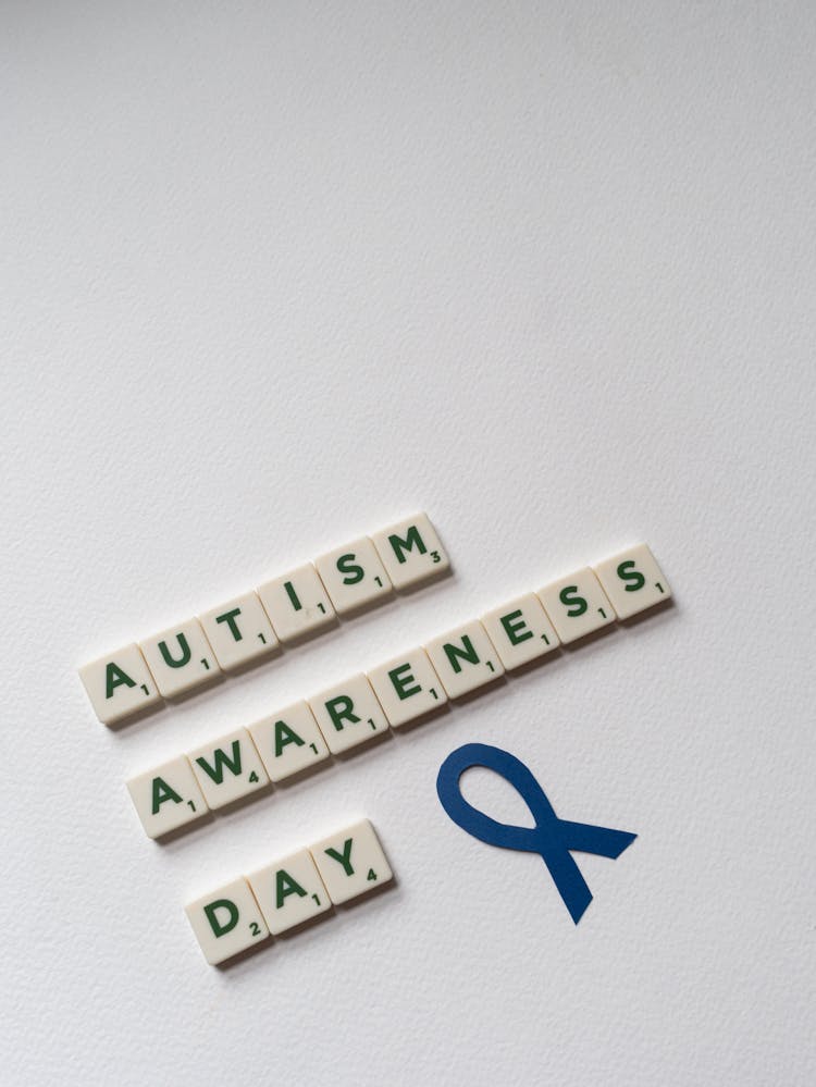 Blue Autism Awareness Ribbon And Scrabble Tiles On White Background