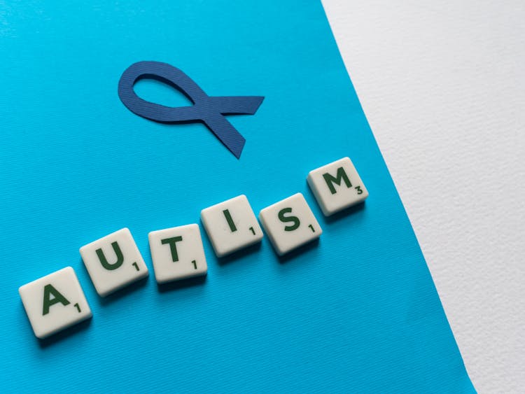 Blue Autism Awareness Ribbon And Scrabble Tiles On Blue Paper