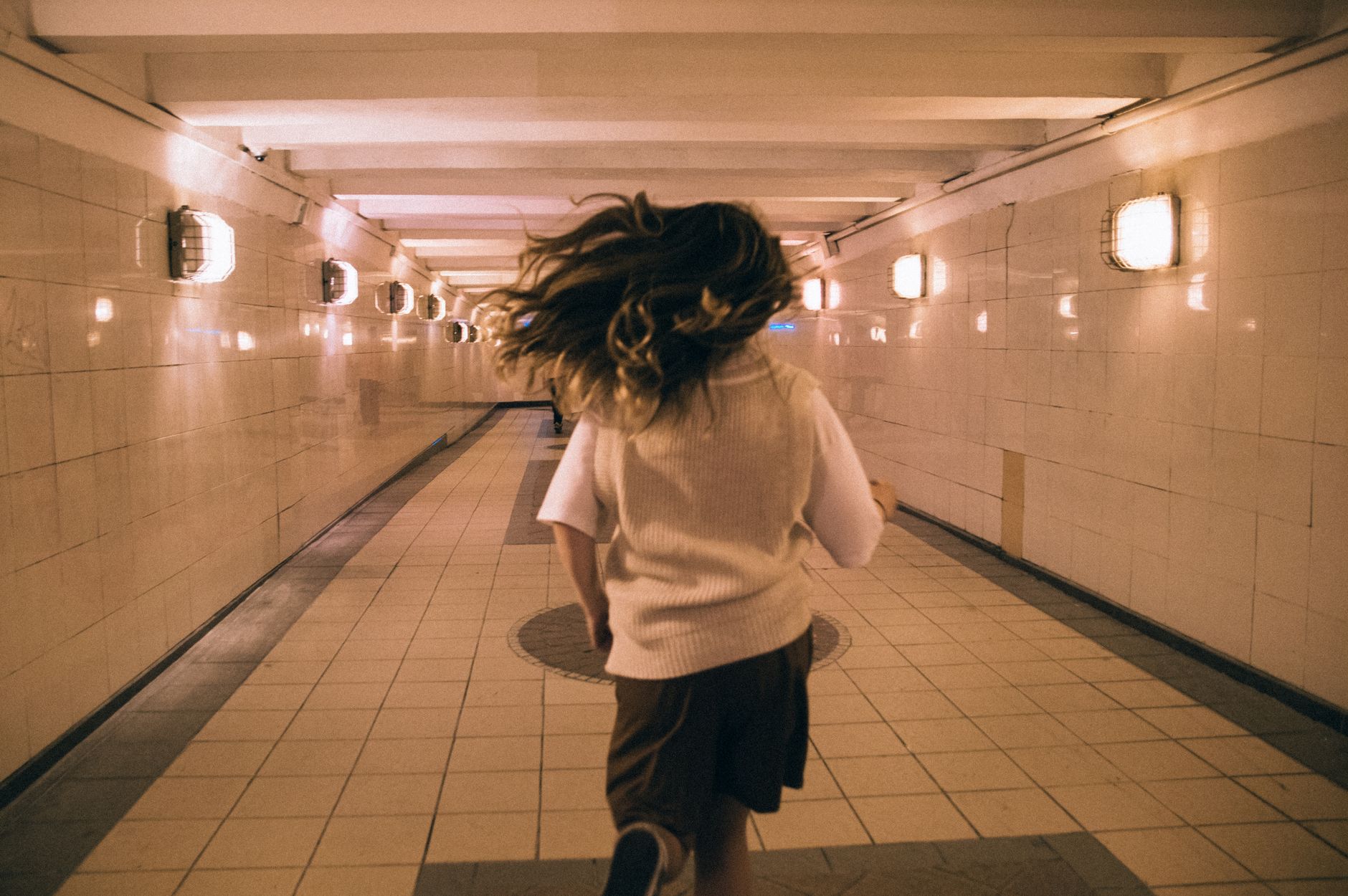 Back view of a woman running in a well-lit underground hallway in Moscow, Russia.