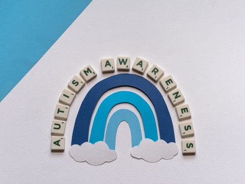 Colorful letter tiles and rainbow paper arranged in an autism awareness composition