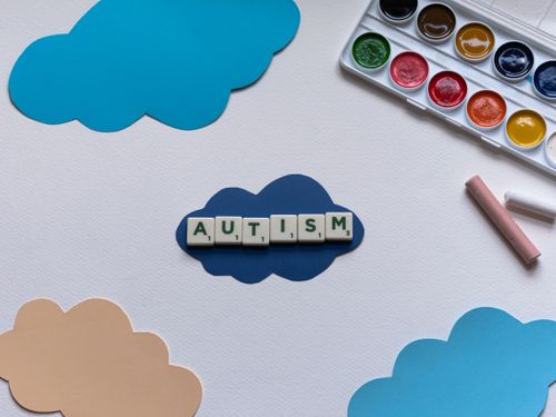 Free Art supplies and scrabble tiles spelling 'autism' on paper clouds, promoting autism awareness. Stock Photo
