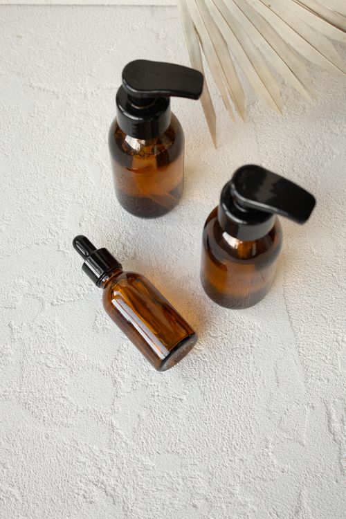 Free Aesthetic brown glass pump and dropper bottles on a textured white surface. Stock Photo