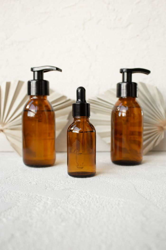 Three amber glass bottles with pump and dropper tops on a textured surface — photo by Liana Horodetska on Pexels
