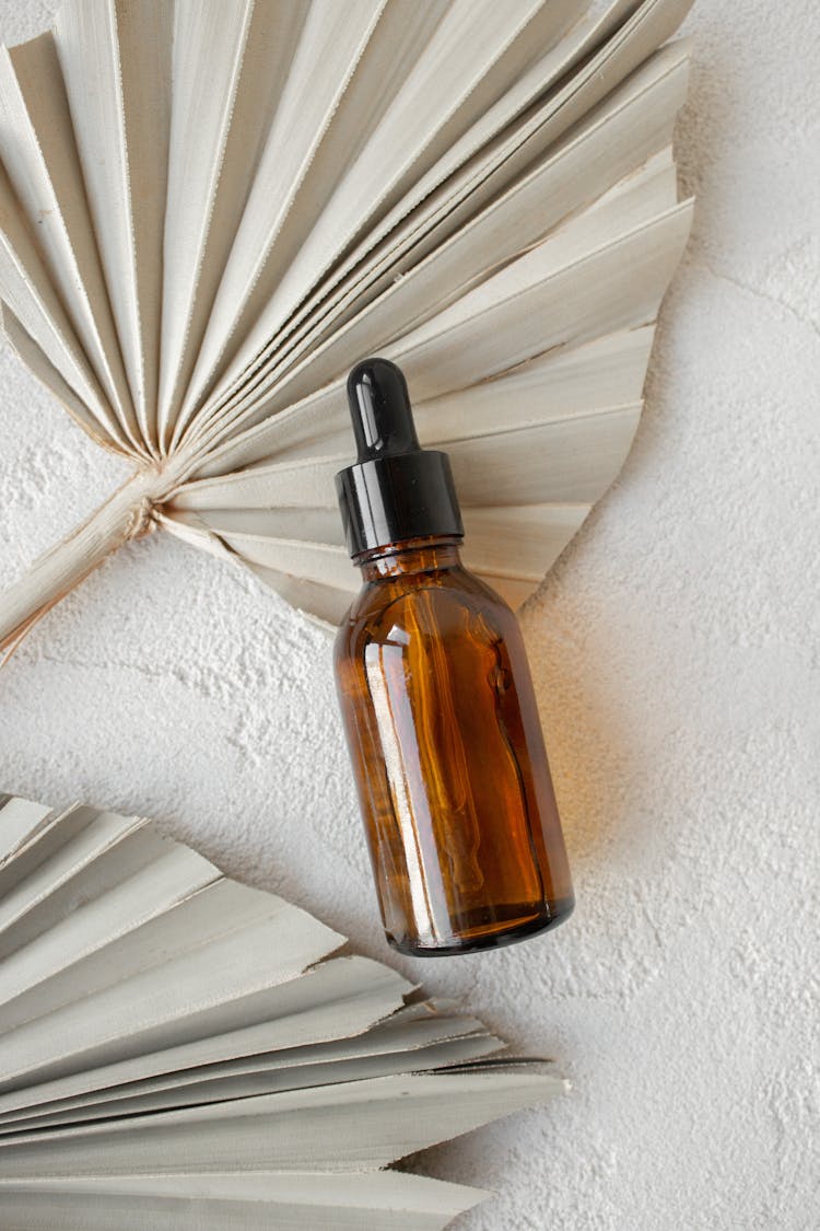 A Brown Squeeze Bottle With Liquid On A White Palm Leaf Fan