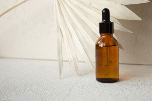 Free Amber glass dropper bottle beside a dried palm fan leaf on a textured surface. Stock Photo