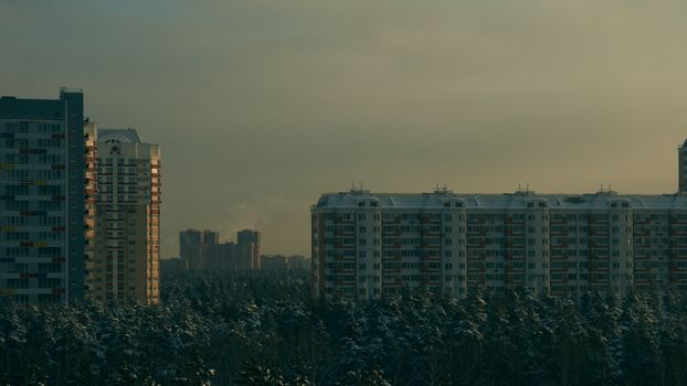 City skyline with residential buildings and snow-covered trees under overcast sky.