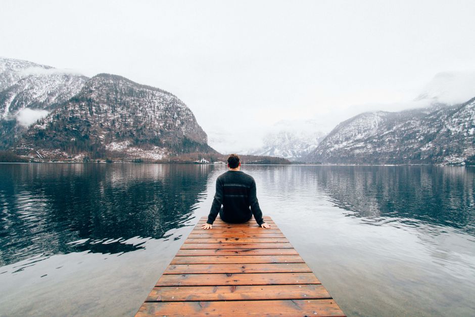 A person sitting on a dock, overlooking snowy mountains and Hallstatt Lake.