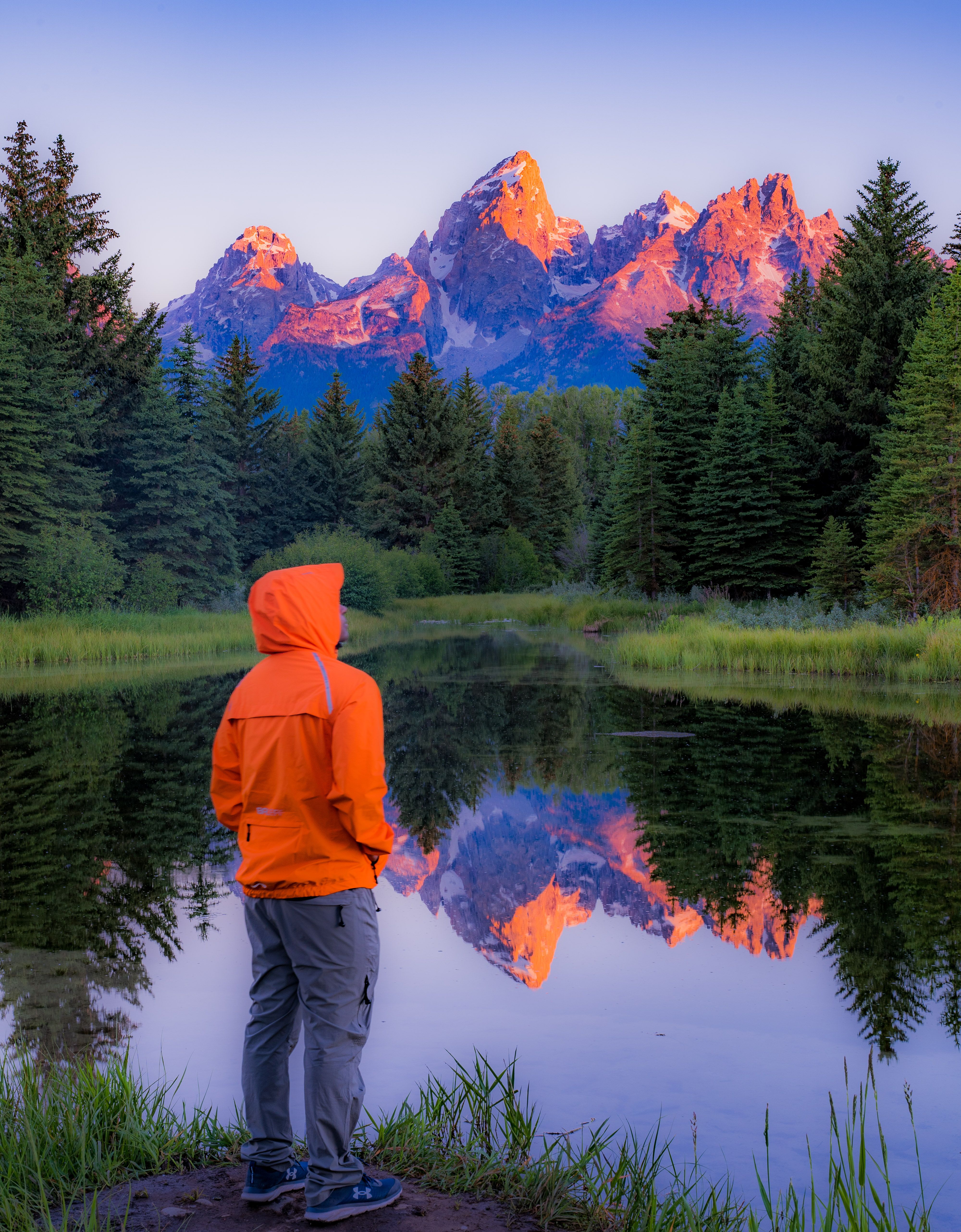 Man in Orange Hoodie Standing on Green Grass Near Lake · Free Stock Photo