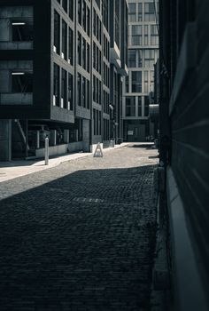 Moody urban alley with shadows, surrounded by modern architecture, creating a dramatic cityscape.
