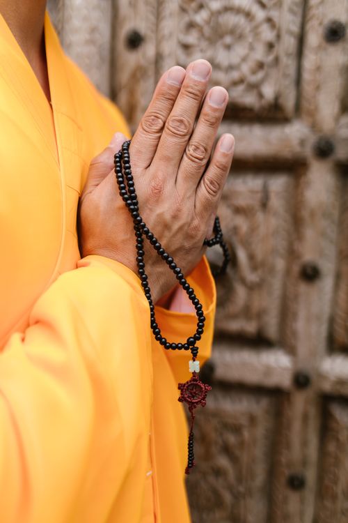 Free A Buddhist monk's hands in prayer holding dark beads against a wooden door. Stock Photo