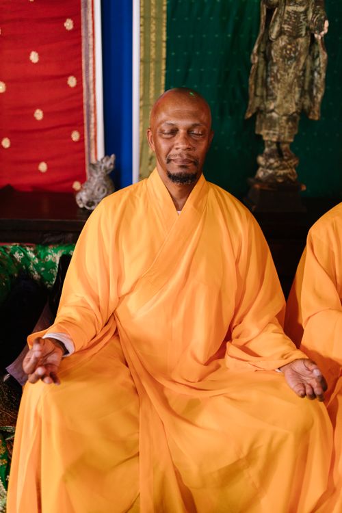 Free A serene Buddhist monk meditating indoors, wearing traditional orange kasaya, surrounded by vibrant decor. Stock Photo