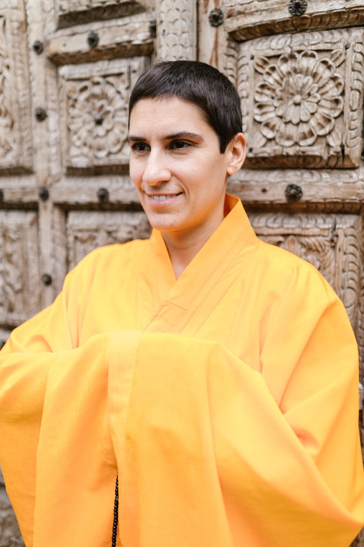 A Man In Yellow Robe Standing Near A Wooden Wall