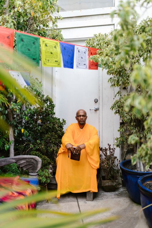 Free A serene scene of a Buddhist monk in orange robes, sitting in a tranquil garden with colorful prayer flags. Stock Photo
