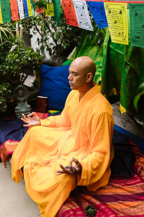 Free A Buddhist monk meditates in a serene setting with colorful prayer flags overhead. Stock Photo