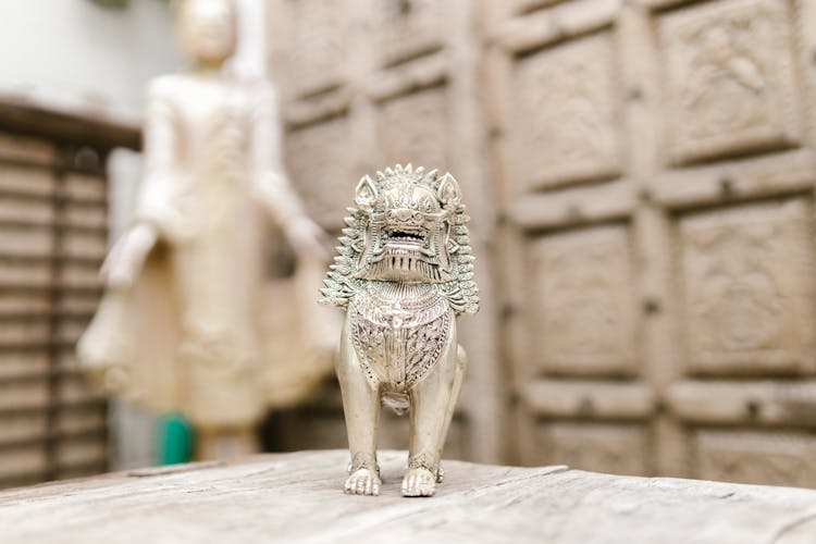 A Gray Miniature Lion Near A Buddha Statue