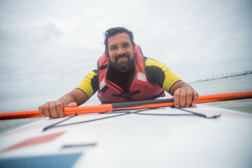 Free Man enjoying paddleboarding adventure on a river in Portugal, wearing a life jacket and smiling. Stock Photo