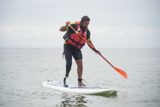 A man with a prosthetic leg enjoys paddleboarding on the ocean, showcasing recreational activities for the disabled.