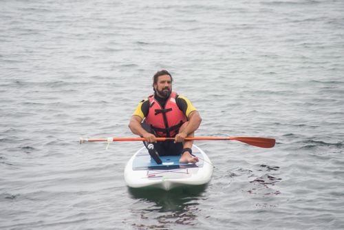 Free Man with a disability paddleboarding on the ocean in Portugal, wearing a red life jacket, showcasing adaptation and adventure. Stock Photo