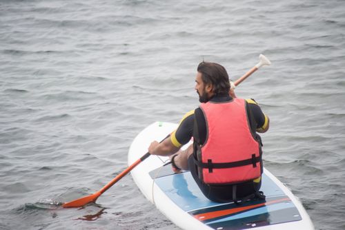 Free Adult man in life vest paddleboarding on calm waters. Perfect for travel and adventure themes. Stock Photo