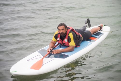 Free Man with prosthetic leg paddleboarding in the ocean, showcasing inclusivity and adventure. Stock Photo