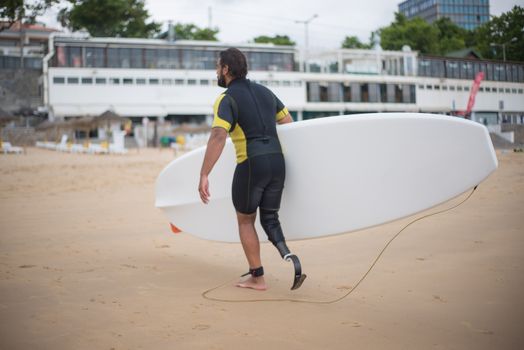 A man with a prosthetic leg carries a surfboard on a beach in Portugal, symbolizing strength and adventure.