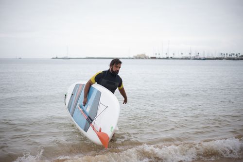 Free A man with a paddleboard on a serene beach in Portugal, enjoying water sports. Stock Photo