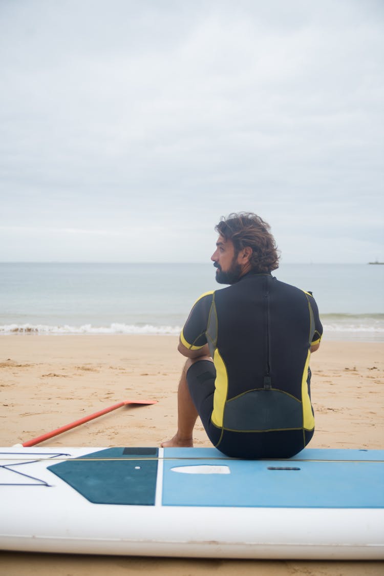 A Man Sitting On Sup Board At The Beach