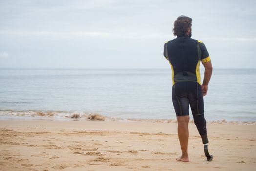 A man with a prosthetic leg walks along a serene beach, embracing adventure.