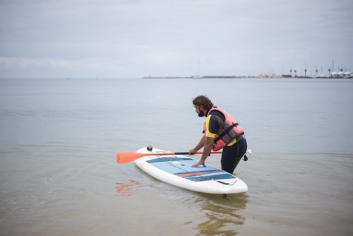Free A man prepares to paddleboard on a calm beach in Portugal under a cloudy sky. Stock Photo