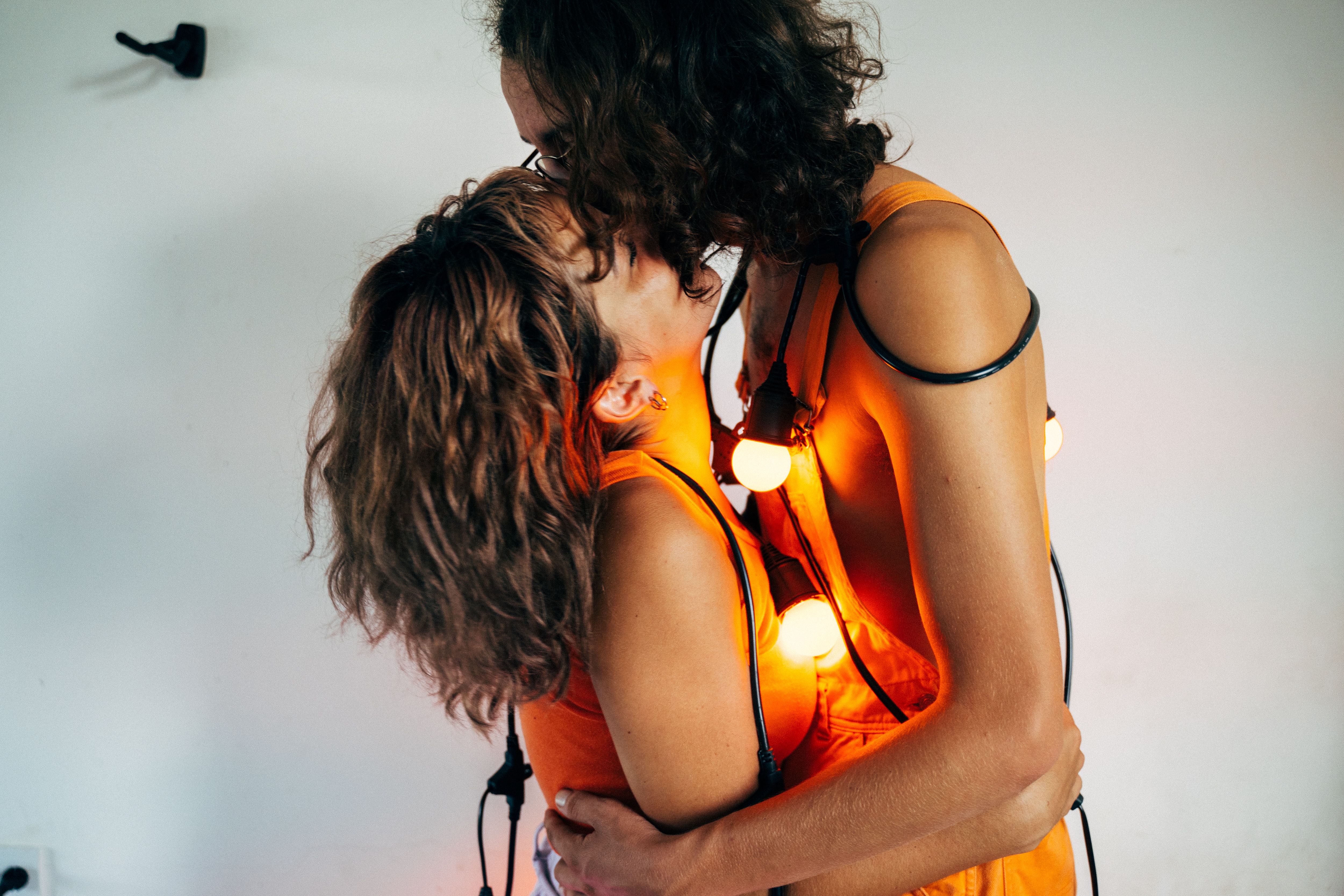 A loving couple embraces, wrapped in string lights, creating a warm romantic glow.