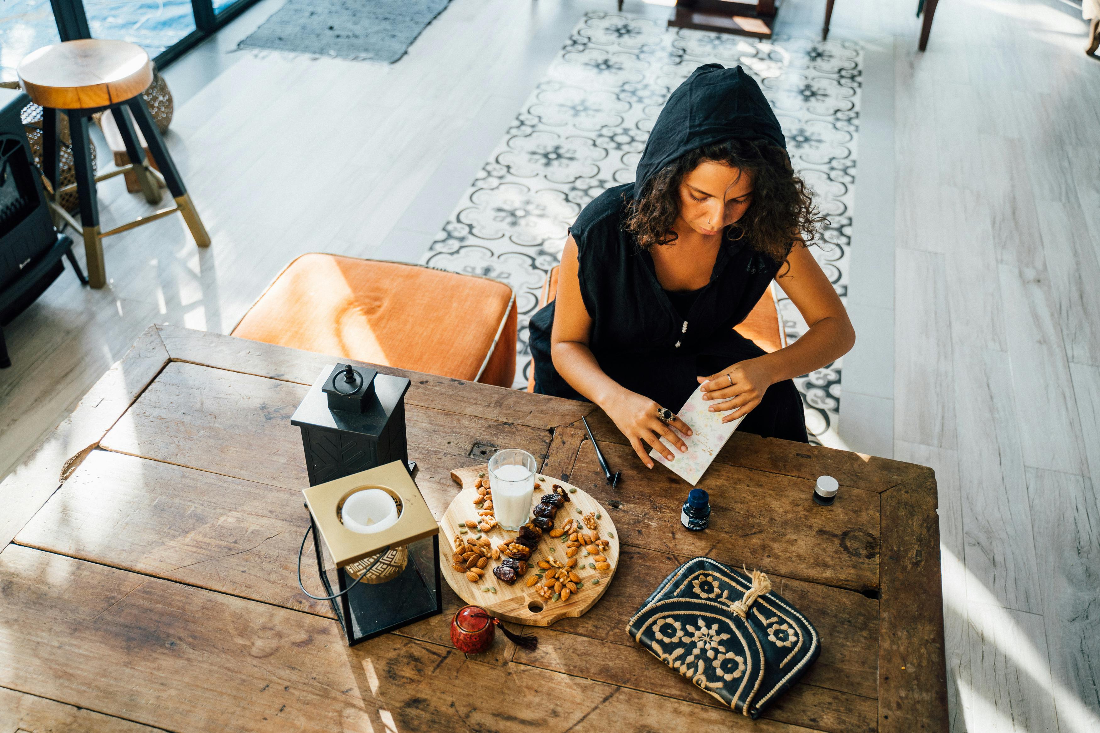 A woman sits at a wooden table preparing food for iftar during Ramadan indoors.