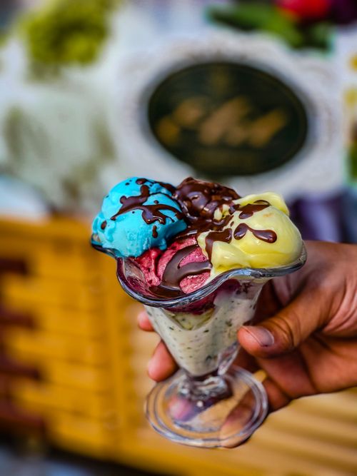 Free Close-up of a vibrant, multi-flavored ice cream sundae held in a glass, showcasing colorful scoops and chocolate drizzle. Stock Photo