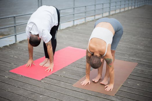 A man and woman practicing yoga together on a wooden dock by the water in Portugal.