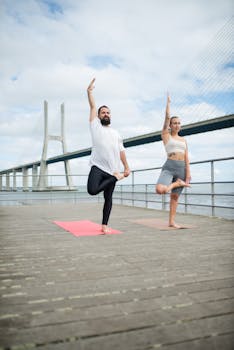 A couple performing yoga poses on a deck near the Vasco da Gama Bridge in Lisbon.