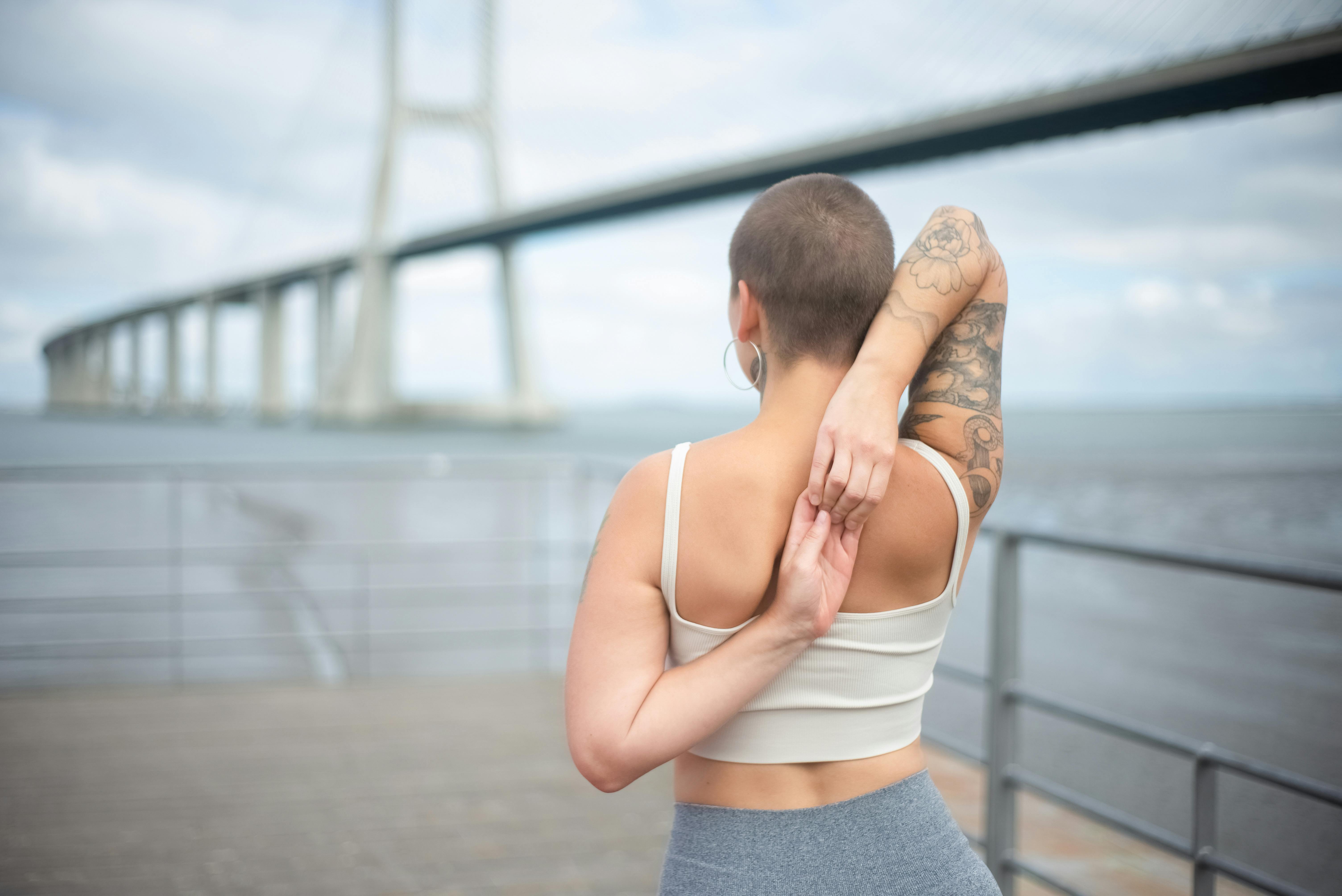 Back view of a woman stretching outdoors by the Vasco da Gama Bridge in Portugal.