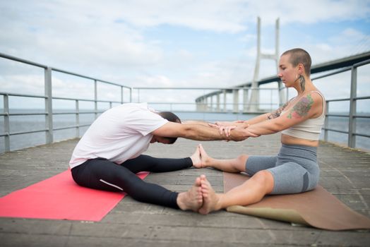 A couple engaging in partner yoga exercises on a bridge in Lisbon, capturing healthy living and fitness vibes.