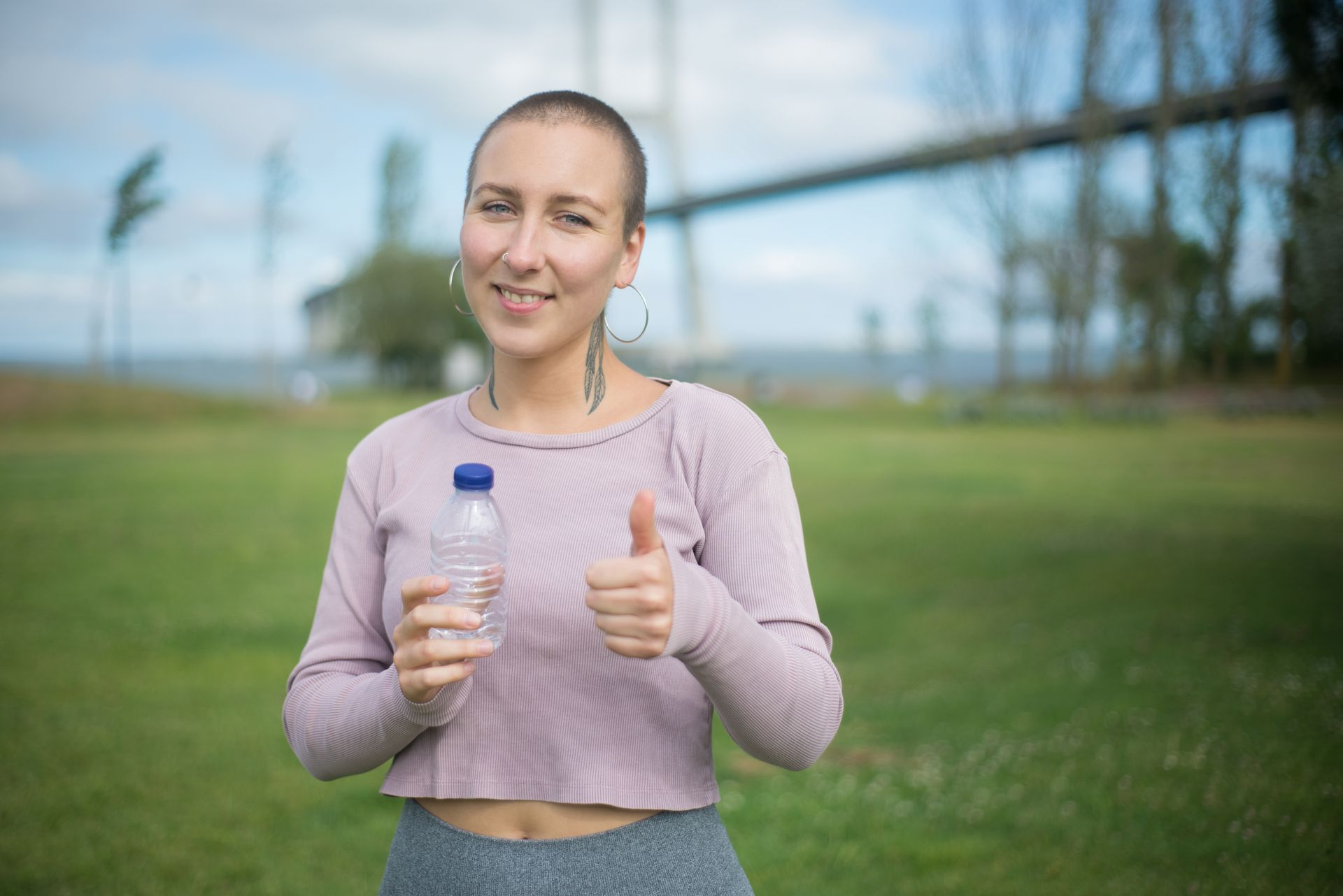 A woman happily gives a thumbs up while enjoying leisure with a water bottle outdoors in Portugal.