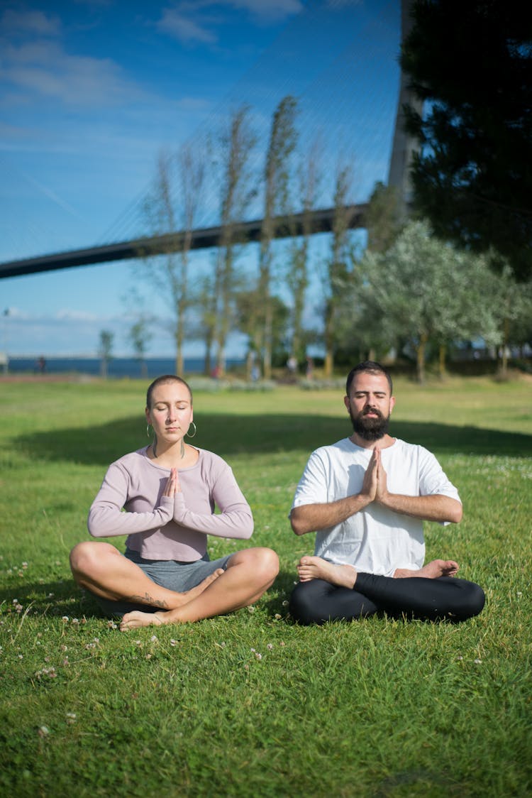 Man And Woman In Meditation Position On Green Grass