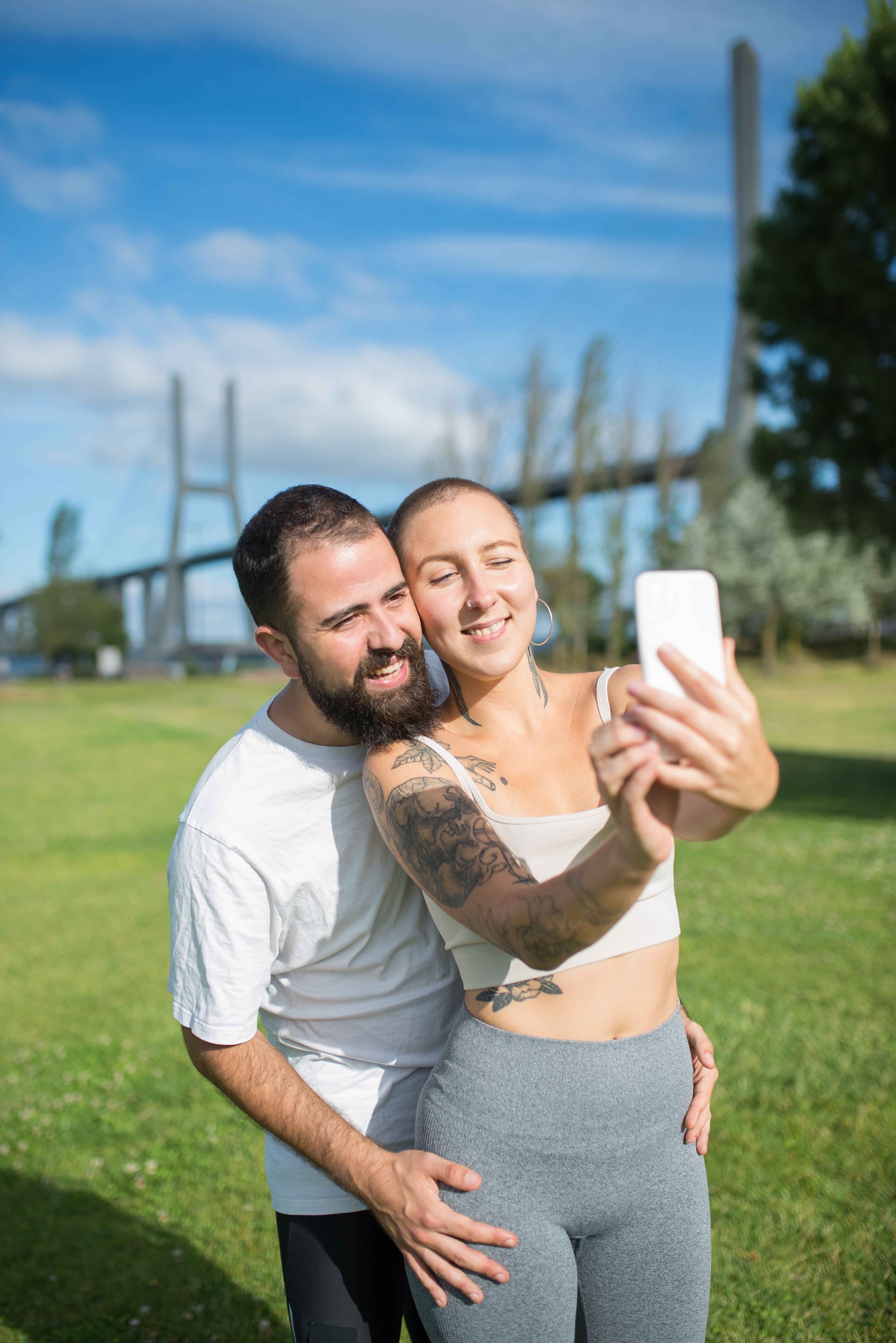 A cheerful couple enjoys a sunny day taking a selfie in a Portuguese park, showcasing love and happiness.