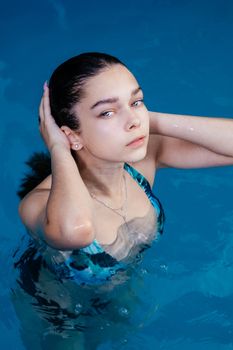 A young woman in swimwear enjoys a relaxing moment in a clear blue pool.